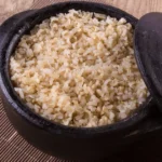 Cooked whole grain brown rice in a black ceramic pot.
