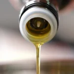 Frying oil being poured from a bottle into a saucepan.