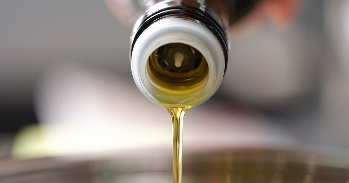 Frying oil being poured from a bottle into a saucepan.
