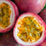 Whole purple passion fruits next to a passion fruit cut into two halves showing the inner yellow pulp.