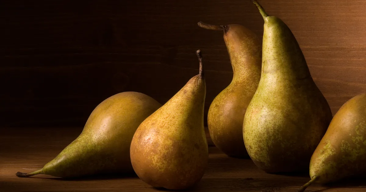 Five pears lined up next to each other on a wooden table.
