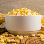 Sweet Corn: Nutrition, Potential Benefits, and Drawbacks Sweet corn in a white bowl with a corn on the cob behind it.