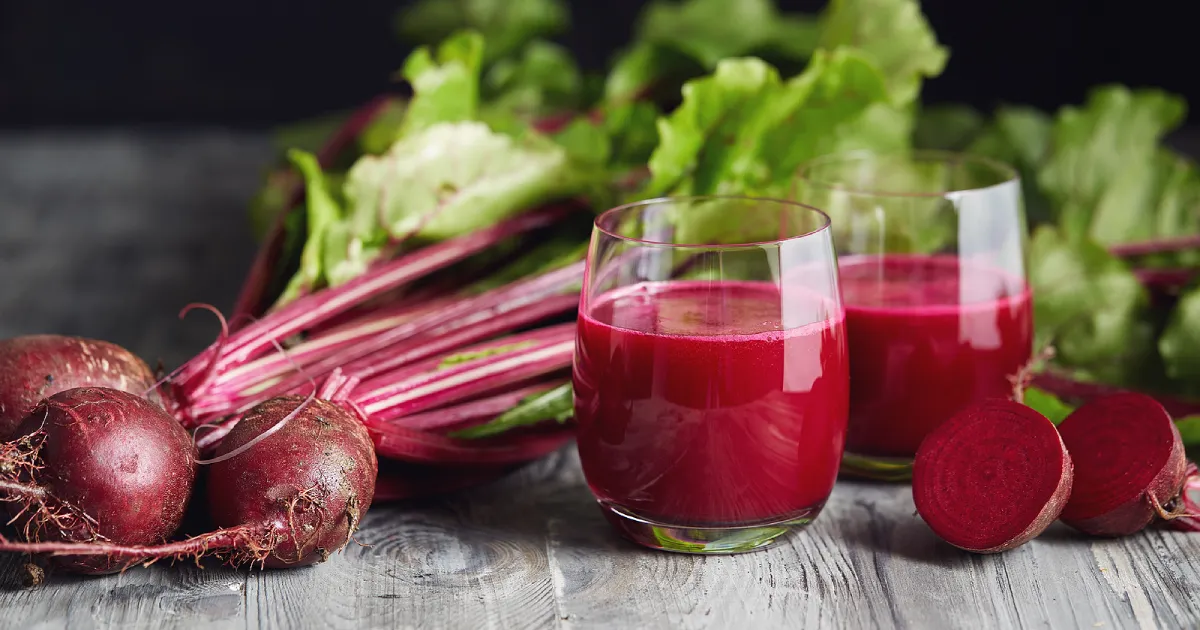 A glass of beet juice next to several whole beets.