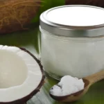 Coconut Oil: Nutrition Profile and Potential Health Effects A spoon of coconut oil next to a jar full of coconut oil.