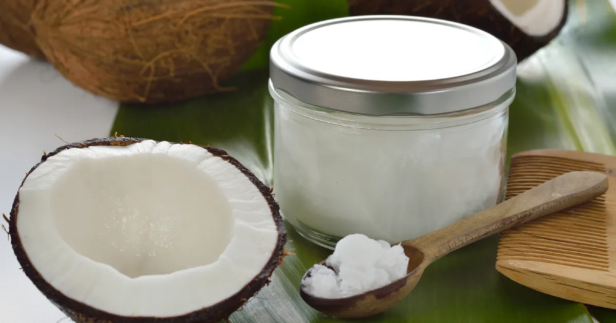 A spoon of coconut oil next to a jar full of coconut oil.