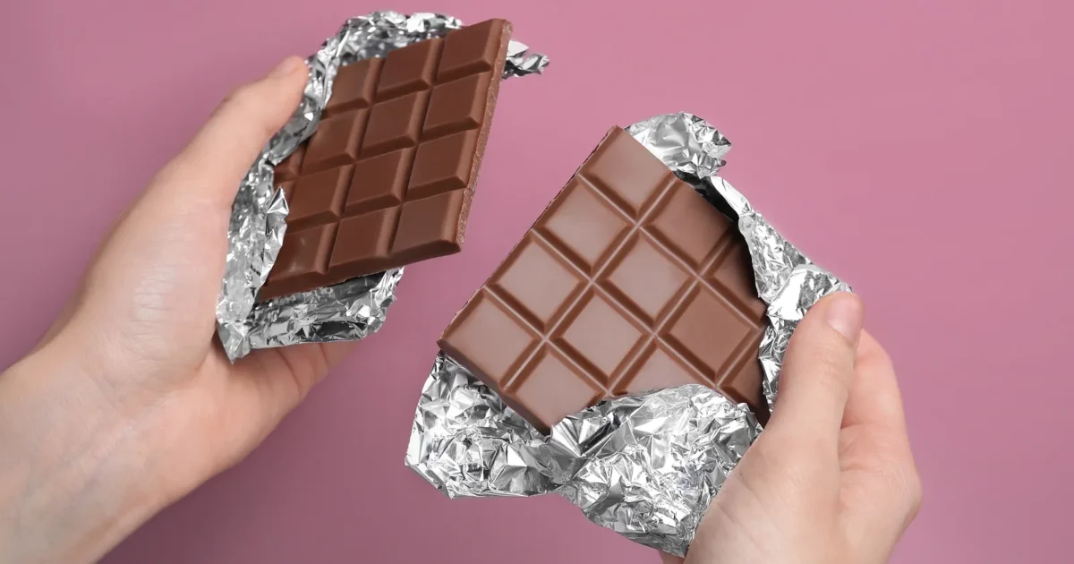 Two hands holding two halves of a milk chocolate bar.