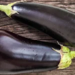 Eggplant: Nutritional Profile, Benefits, and Drawbacks Two whole, fresh eggplants on a wooden surface.