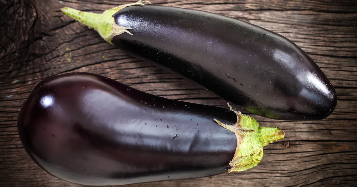Two whole, fresh eggplants on a wooden surface.