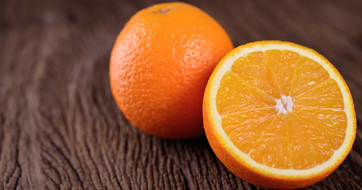 A whole, fresh navel orange next to a half piece of orange.