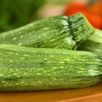 Zucchini: Key Nutrients, Health Benefits and Nutrition Profile Three whole zucchinis on a wooden chopping board.