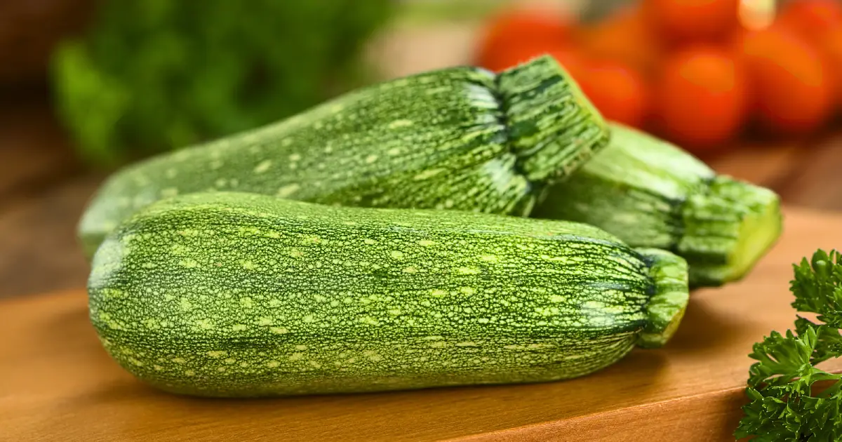 Three whole zucchinis on a wooden chopping board.