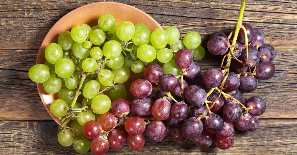 Bunches of green and red grapes on a wooden surface.