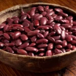 A wooden bowl full of raw red kidney beans.