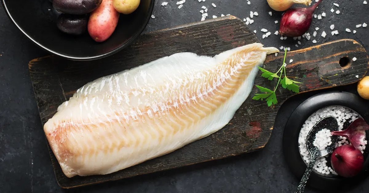 A white fillet of cod fish on a black wooden board.