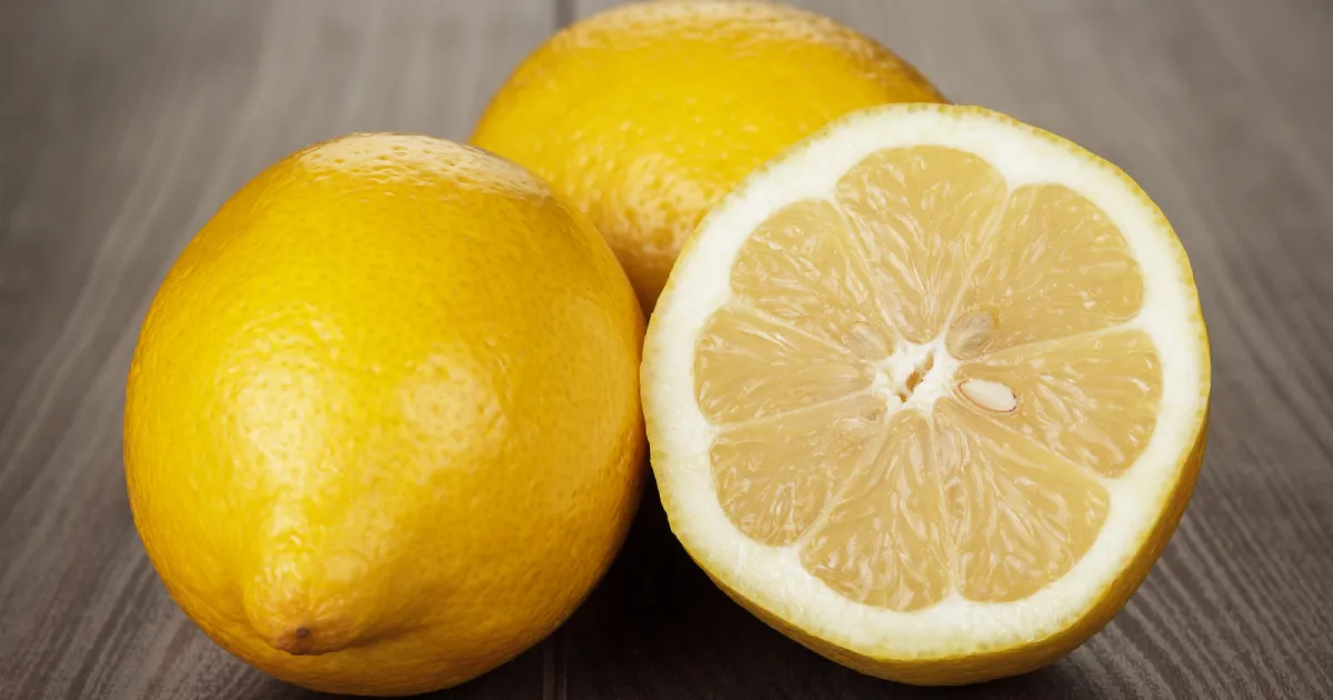 A whole lemon next to a half lemon on a wooden surface.